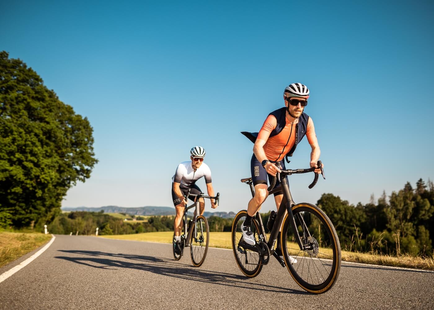 Two guys in road cycling outfits riding through a country road.