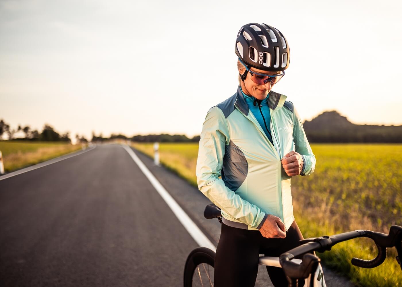 A woman is putting on a wind breaker for road riding.